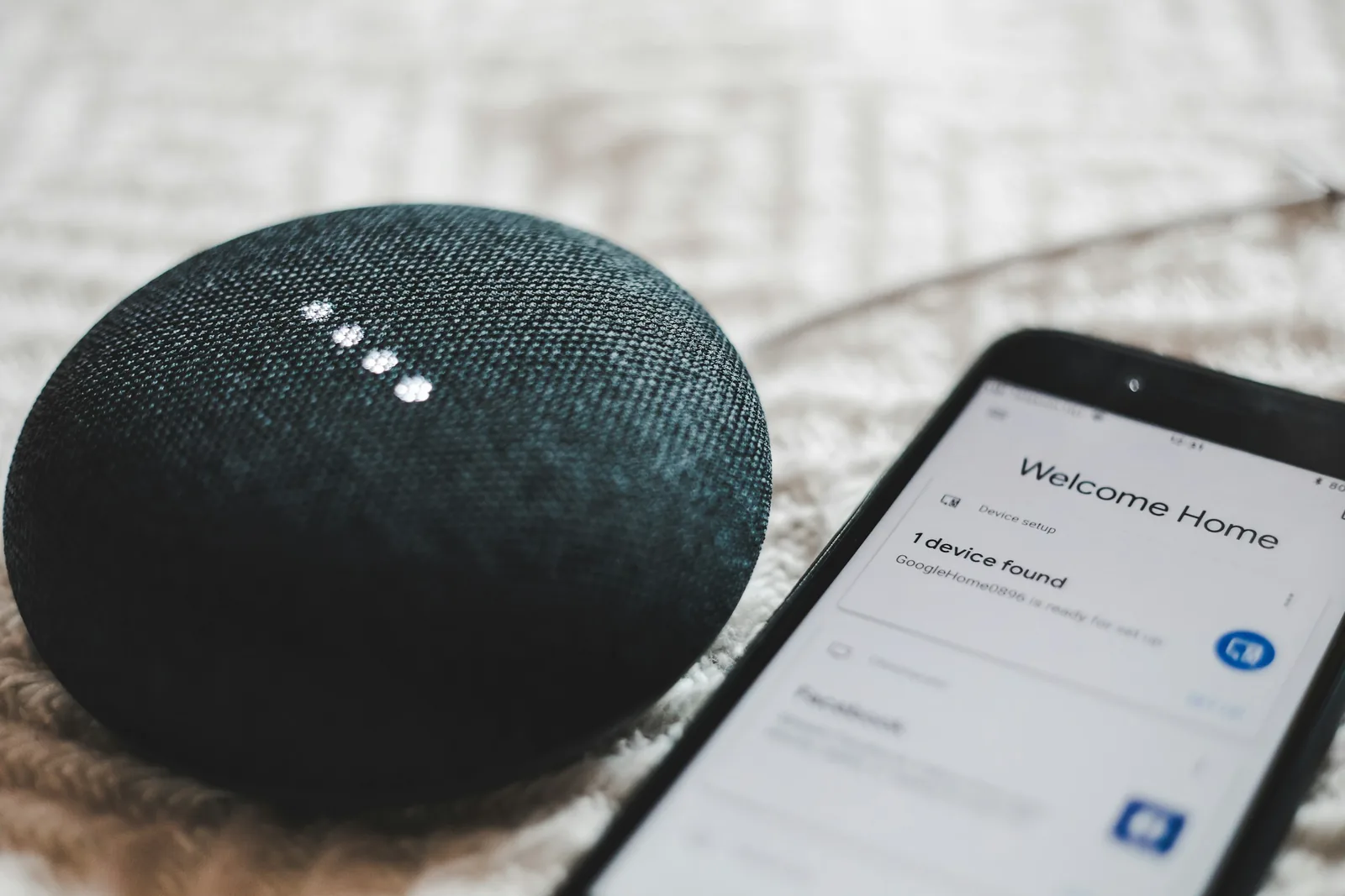A small smart speaker next to a phone showing a home app