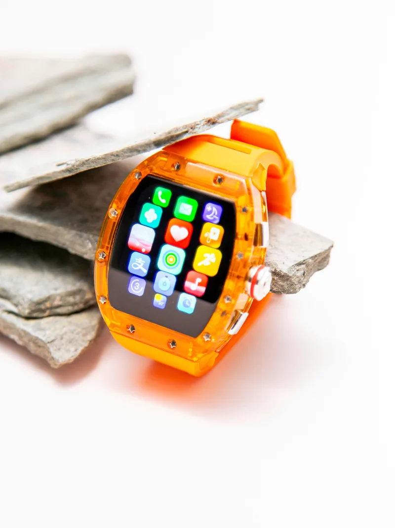 A bright orange smartwatch with app icons on its screen, resting on flat stones