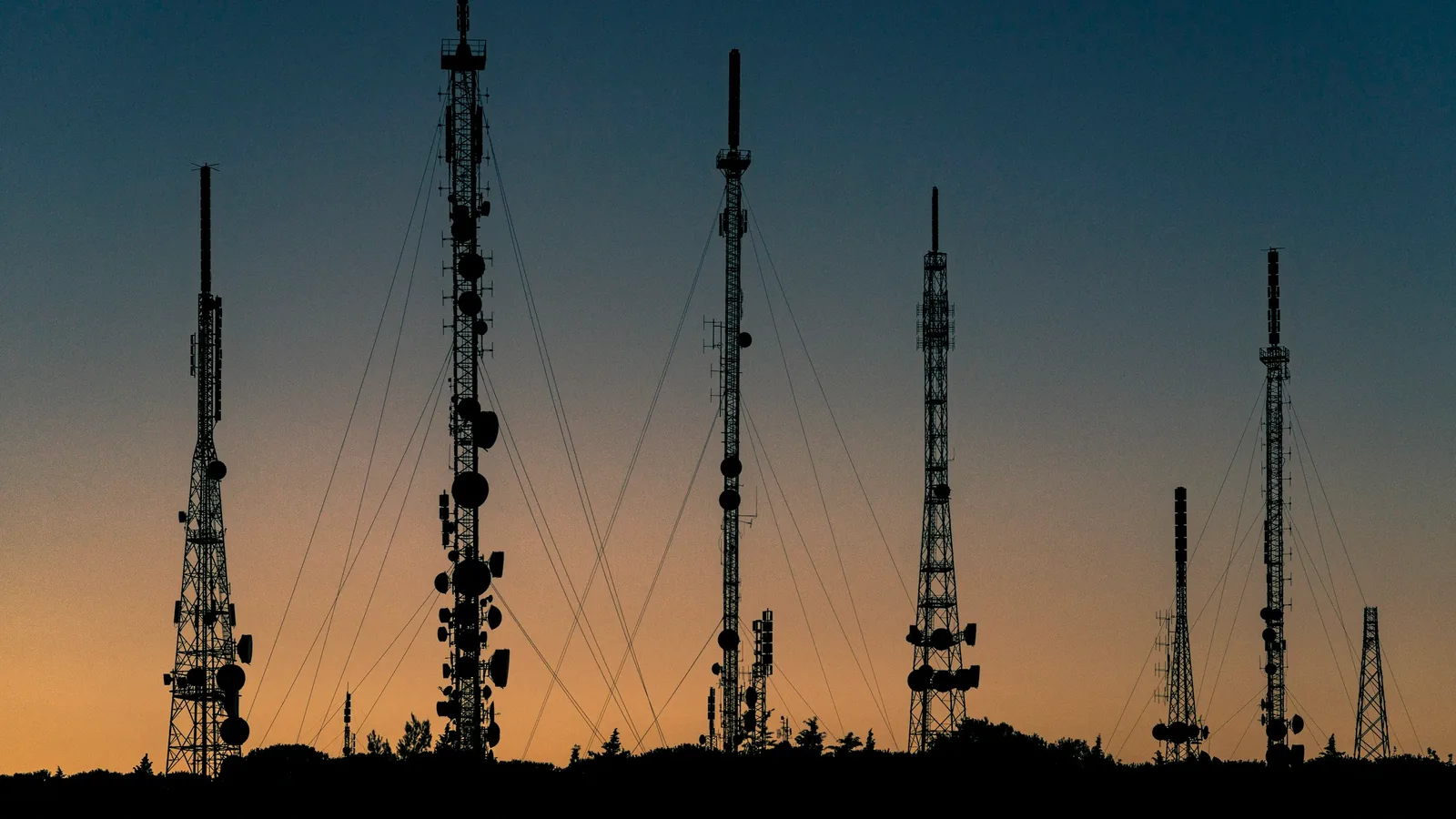 Radio and cellular towers silhouetted against a sunset